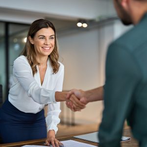 Business handshake concept. Happy middle aged professional woman manager and male client or partner shaking hand expressing trust in b2b partnership at meeting in corporate office. Hiring, onboarding.